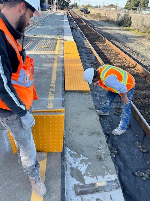 Finishing a fresh concrete platform edge alongside active rail tracks